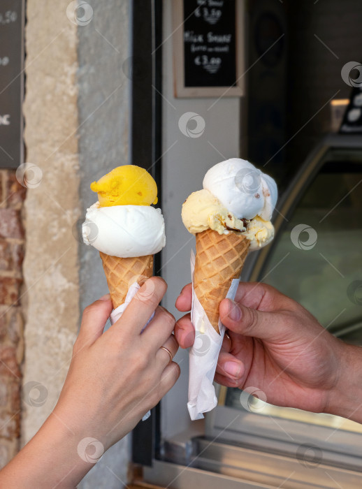 Скачать Смешайте мороженое в вафельных рожках. Мужчина и женщина держат мороженое за руки на фоне магазина. Аппетитный фон с десертом. фотосток Ozero