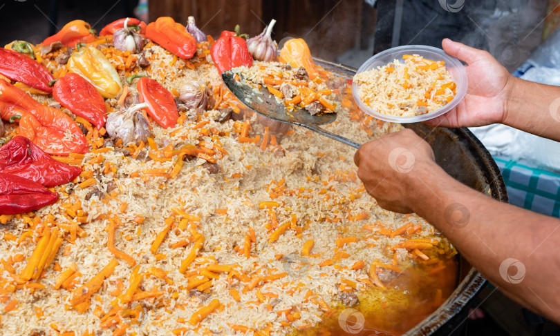 Скачать Повар перекладывает горячий вкусный плов из казана в пластиковую тарелку. Азиатская уличная еда фотосток Ozero