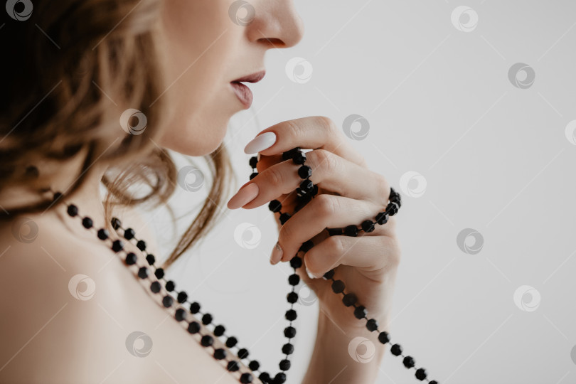 Скачать Привлекательная кавказская девушка в черном платье накручивала на пальцы нитку бус фотосток Ozero