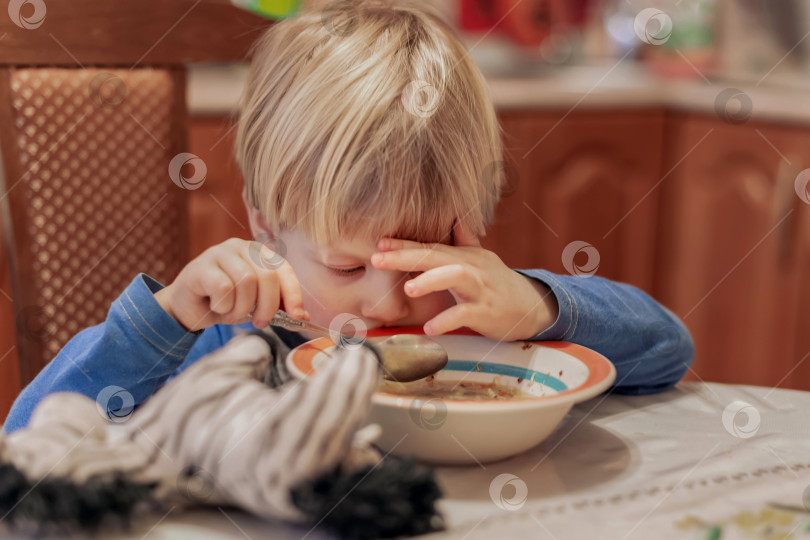 Скачать Маленький грустный мальчик держит ложку, но не хочет есть суп фотосток Ozero