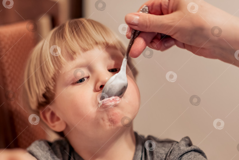 Скачать Мать кормит белокурого мальчика с ложечки фотосток Ozero