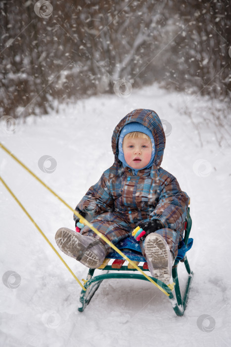 Скачать Маленький мальчик катается на санках по заснеженной дороге зимним днем фотосток Ozero