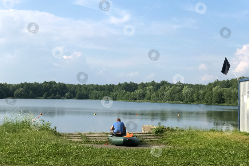 Скачать Мужчина сидит на борту надувной лодки на берегу озера летним днем фотосток Ozero
