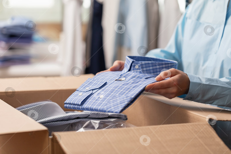 Скачать Продавец кладет сложенную рубашку в коробку для отправки клиенту, женщина отправляет товар на рынки фотосток Ozero