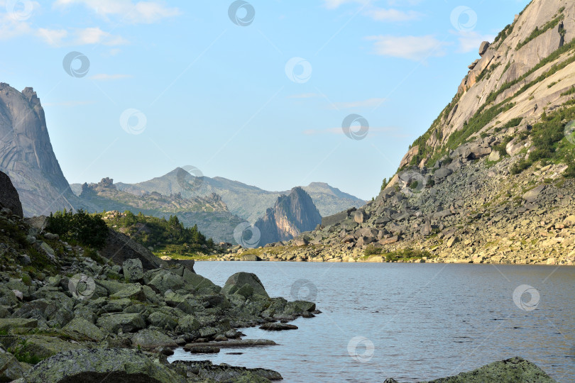 Скачать Скалистый берег большого озера у подножия высокой скалы солнечным летним днем. фотосток Ozero