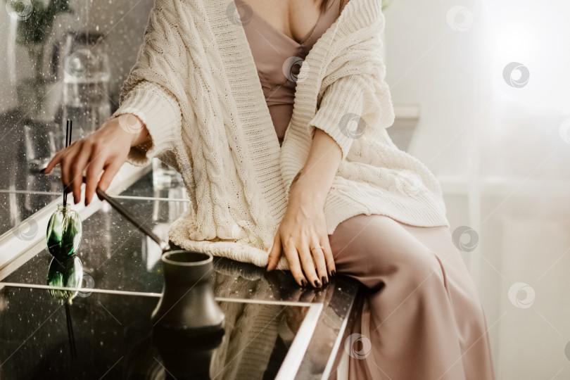 Скачать Молодая привлекательная женщина в вязаном белом свитере сидит на кухонном столе и готовит утренний кофе фотосток Ozero