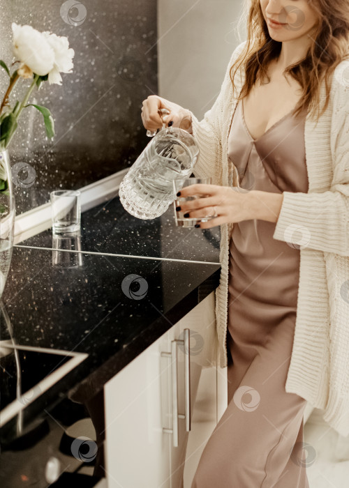 Скачать женщина стоит на кухне и наливает воду в стакан из стеклянного графина фотосток Ozero