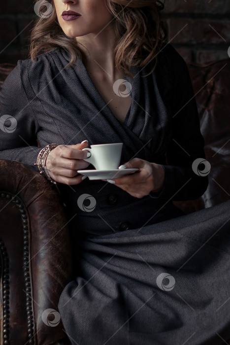 Скачать Женщина в темном платье сидит в кресле и держит в руках кофейную чашку фотосток Ozero