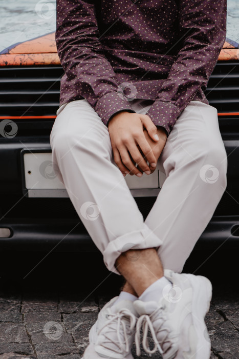 Скачать стильно одетый молодой человек сидит на капоте автомобиля фотосток Ozero
