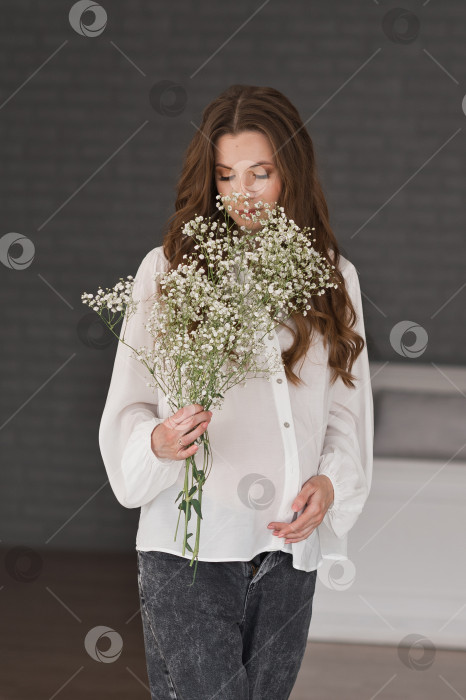 Скачать Беременная девушка в белой свободной блузке с букетом полевых цветов фотосток Ozero