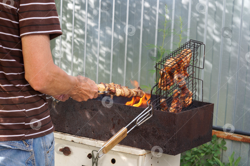Скачать Пенсионер жарит на самодельном мангале шашлык из мяса на шампурах и ножки курицы на решетке фотосток Ozero