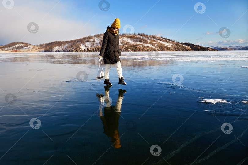 Скачать Молодая девушка идет по льду замерзшего озера. Он держит в руках коньки. фотосток Ozero