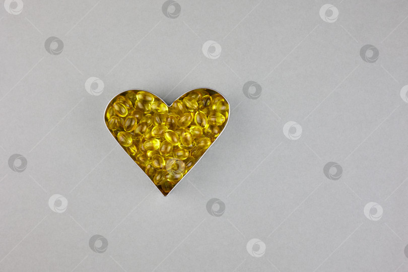 Скачать Желтые капсулы с витамином D3 на сером фоне, выложенные в форме сердца. фотосток Ozero
