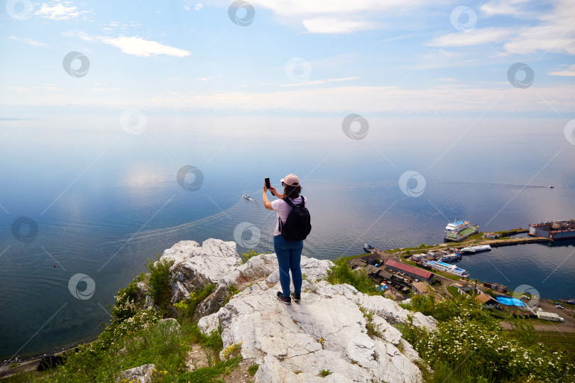 Скачать Женщина-путешественница стоит на скале недалеко от порта Байкал и фотографирует озеро Байкал фотосток Ozero