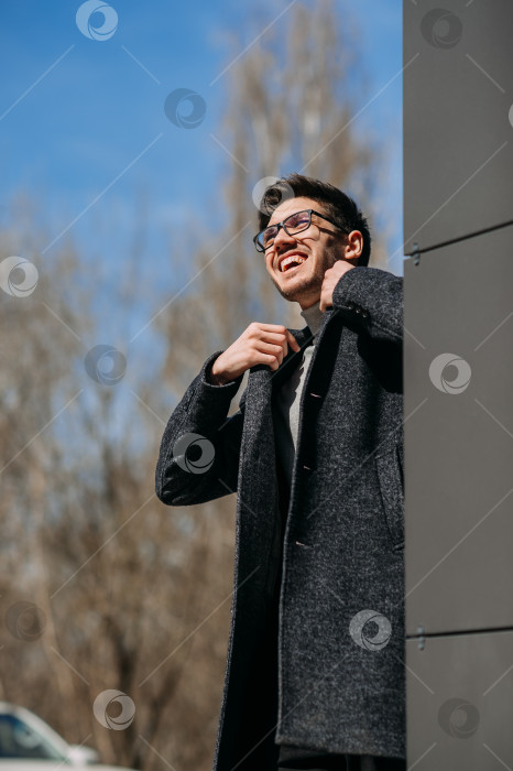 Скачать Мужчина в очках на улице. Он улыбается и одет в черное пальто. 4 фотосток Ozero