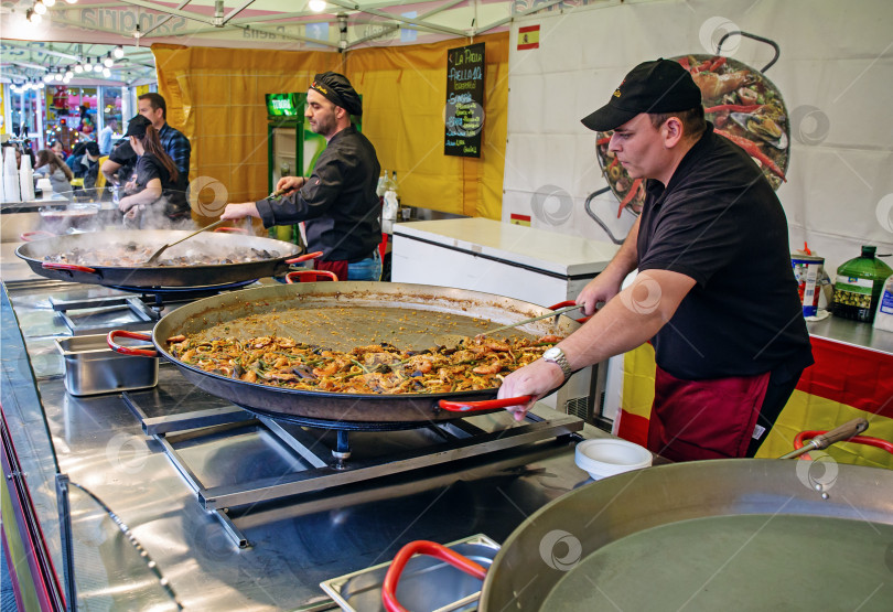 Скачать Шеф-повара готовят ризотто с различными морепродуктами на больших сковородках на рынке в Генуе фотосток Ozero