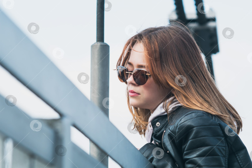Скачать Молодая девушка в стильных очках и кожаной куртке на подвесном мосту фотосток Ozero