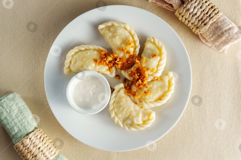 Скачать На белой тарелке представлено множество восхитительных пельменей, идеально сочетающихся с сочной миской ароматного соуса. фотосток Ozero