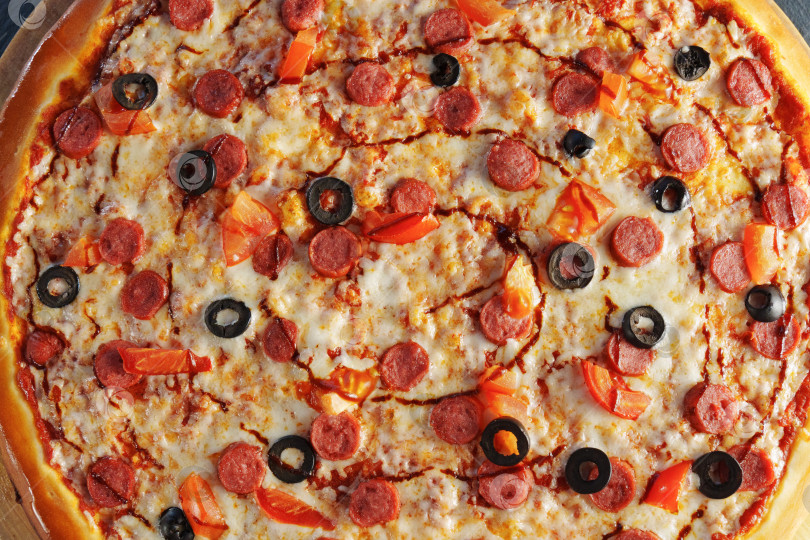Скачать Пицца пепперони, украшенная черными оливками и ломтиками красного болгарского перца, подается на круглой деревянной доске фотосток Ozero