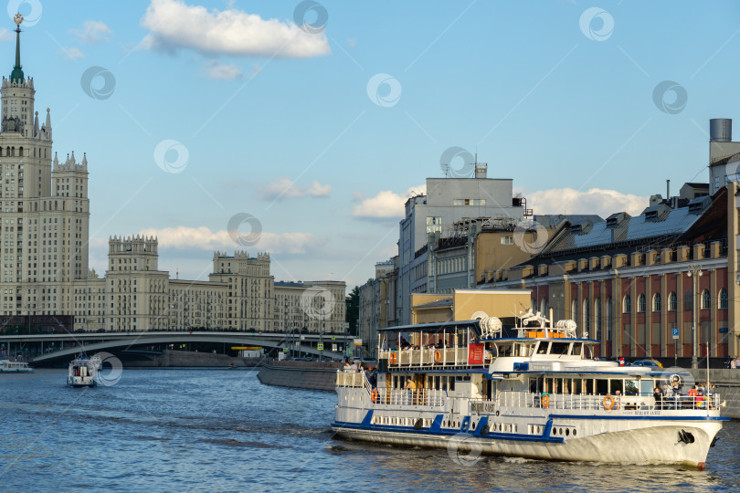 Скачать Прогулочные катера с людьми на борту плывут по Москве-реке на фоне Раушской набережной. Летний воскресный вечер фотосток Ozero