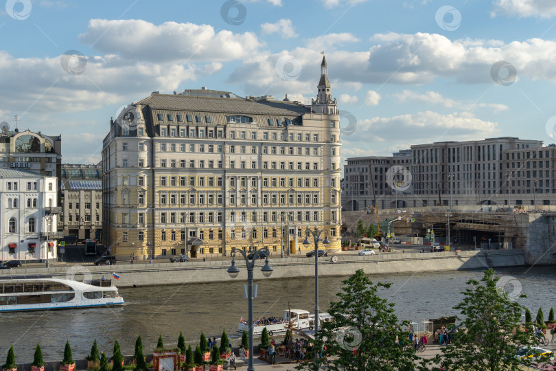 Скачать Москва, Россия - 16 июня 2019 года: Вид на Раушскую набережную с красивым зданием отеля "Балчуг Кемпински" из парка Зарядье. Прогулочные катера плывут по Москве-реке. Летний воскресный вечер фотосток Ozero