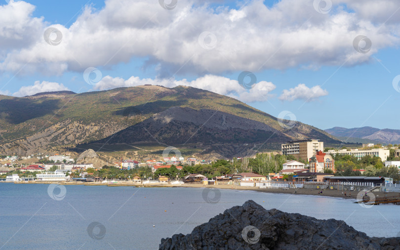 Скачать Живописный крымский пейзаж с голубой водой Черного моря и древней генуэзской крепостью на фоне гор. Туристическая достопримечательность города-курорта Судак. Судак, Крым, Россия – 2 октября 2019 г. фотосток Ozero