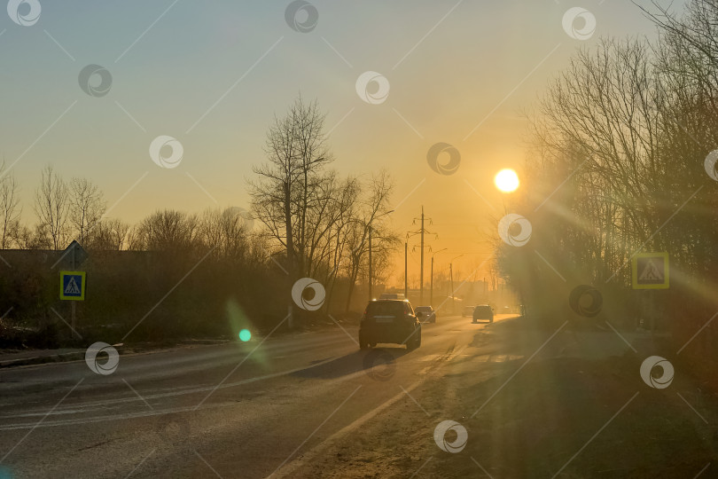 Скачать Автомобили едут по дороге в лучах заходящего солнца, освещая городской пейзаж фотосток Ozero