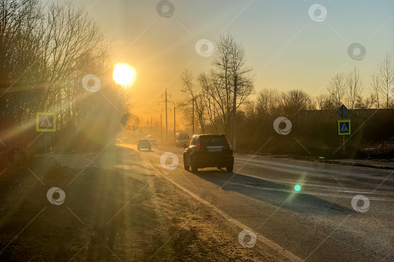 Скачать Автомобили едут по дороге в лучах заходящего солнца, освещая городской пейзаж фотосток Ozero