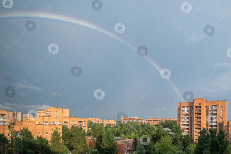 Скачать Радуга после грозы в голубом небе над многоэтажными зданиями фотосток Ozero