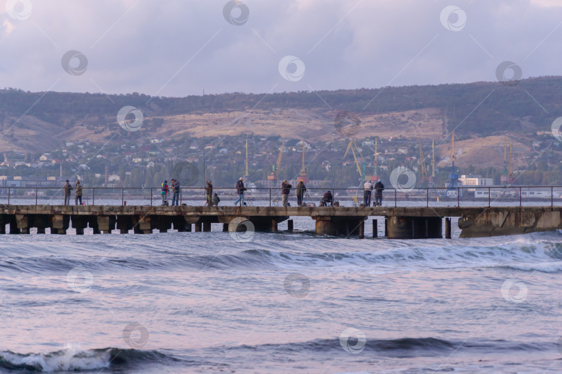 Скачать Рыбак на пирсе Феодосии ловит рыбу в Черном море перед восходом солнца. Красочное рассветное небо. фотосток Ozero