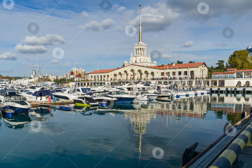 Скачать Сочи, Россия - 23 ноября 2020 года: Морской торговый порт Сочи. Центр города с острием башни главного здания Морского вокзала. Корабли, яхты и катера на голубой глади Черного моря. фотосток Ozero