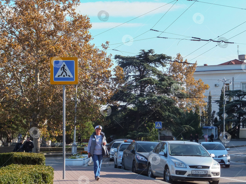 Скачать Женщина в матросской футболке прогуливается осенью по Севастополю мимо припаркованных легковых автомобилей фотосток Ozero