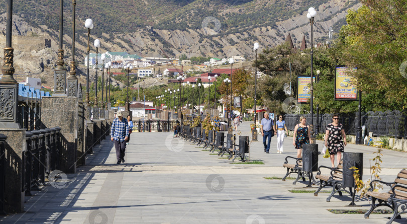 Скачать Люди прогуливаются по красивой набережной крымского курортного города Судак. Набережная Черного моря - любимое место семейных прогулок и туристов. Судак, Крым, Россия – 2 октября 2019 г. фотосток Ozero