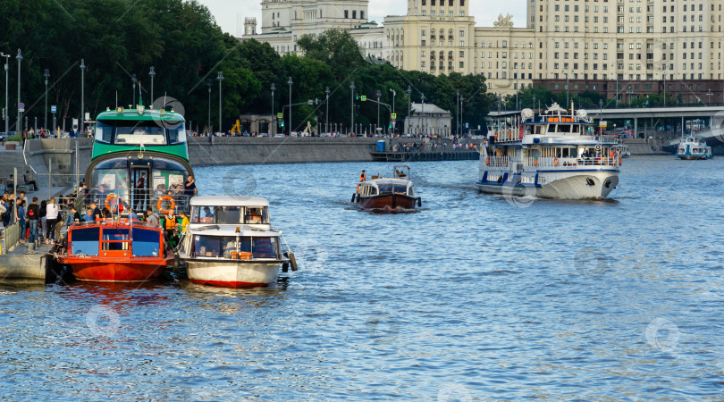 Скачать Прогулочные катера с людьми на борту плывут по Москве-реке на фоне Раушской набережной. Летний воскресный вечер фотосток Ozero