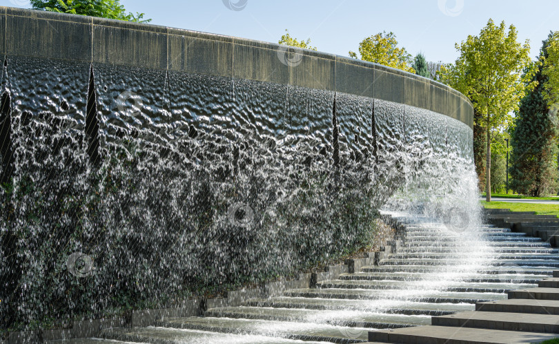 Скачать Водопад ручьями стекает в гранитное русло искусственной реки. Фонтан в виде огромной чаши. Общественный ландшафтный городской парк Краснодара или "Парк Галицкого" для отдыха и прогулок солнечной осенью 2020 года фотосток Ozero