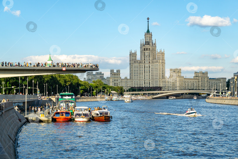 Скачать Плавучий мост в парке Зарядье над Москвой-рекой. Вид на небоскреб на Котельнической набережной на закате с прогулочных катеров. фотосток Ozero