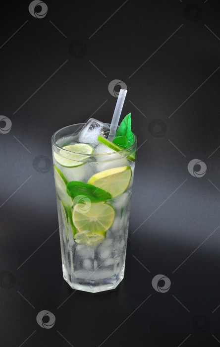 Скачать Высокий стакан лимонада со льдом и соломинками на черном фоне, с ломтиками лимона, лайма и листьями. фотосток Ozero