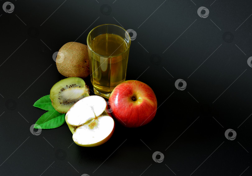 Скачать Высокий стакан фруктового сока на черном фоне, рядом с ломтиками спелого киви и красным яблоком. фотосток Ozero