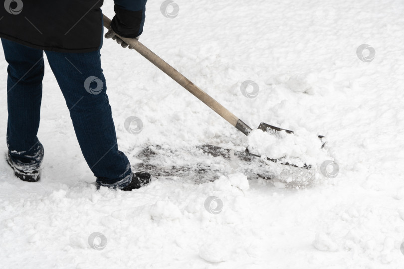 Скачать Мужчина расчищает свежевыпавший снег надежной железной лопатой с деревянной ручкой фотосток Ozero