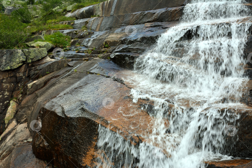 Скачать Быстрый поток воды низвергается каскадом по каменистым ступеням в солнечный летний день. фотосток Ozero