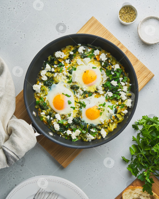 Скачать Зеленая шакшука с яйцами, шпинатом, соленым сыром из овечьего молока, сельдереем и перцем на сковороде фотосток Ozero