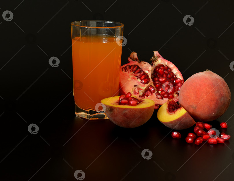Скачать Стакан сока из смеси фруктов и кусочков спелого персика и разломанного плода граната на черном фоне. фотосток Ozero
