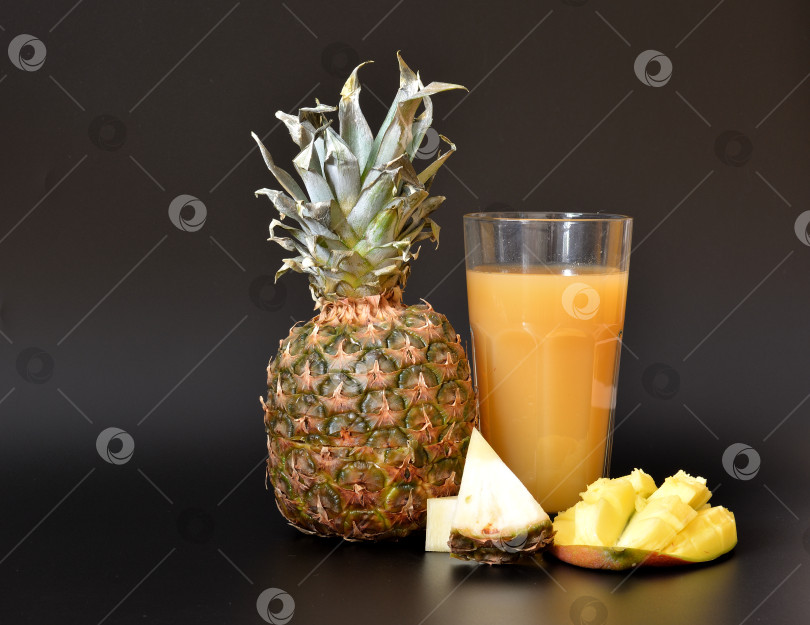 Скачать Смесь фруктовых соков в высоком граненом стакане на черном фоне, рядом с кусочками спелого ананаса и манго. фотосток Ozero