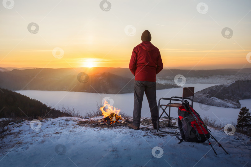 Скачать мужчина стоит у костра и наслаждается закатом на вершине горы. фотосток Ozero