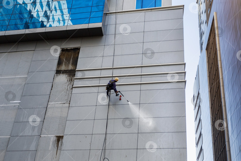Скачать Рабочий моет фасад стены на высоте современного здания. фотосток Ozero