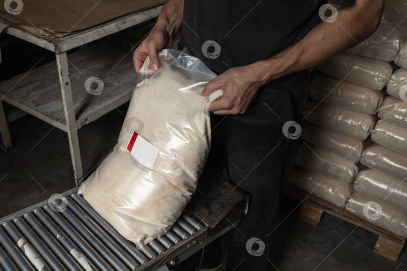 Скачать Работник в грязном цехе занимается упаковкой продуктов питания, снимает со сборочной линии полный пакет сахара, концепция контрафактного производства продуктов питания фотосток Ozero