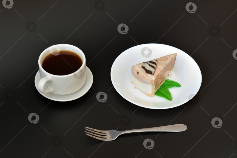 Скачать Кусочек сливочного чизкейка с мятой на тарелке, чашка горячего черного кофе и вилка на черном фоне. фотосток Ozero