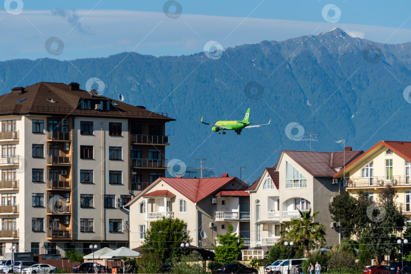 Скачать Airbus A320-271N пролетает над домами на фоне заснеженных вершин Кавказских гор. Крупный план. S7 Airlines. Крупный план. Шасси и закрылки самолета выпущены. фотосток Ozero