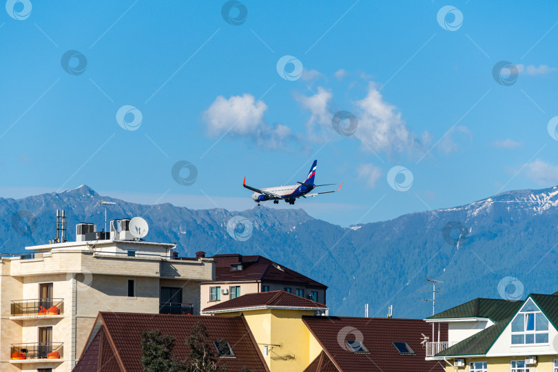 Скачать Boeing 737-8LJ(WL) пролетает над домами на фоне заснеженных вершин Кавказских гор.Аэрофлот - Российские авиалинии. У самолета выпущены шасси и закрылки. Сочи, Россия - 18 мая 2021 г. фотосток Ozero
