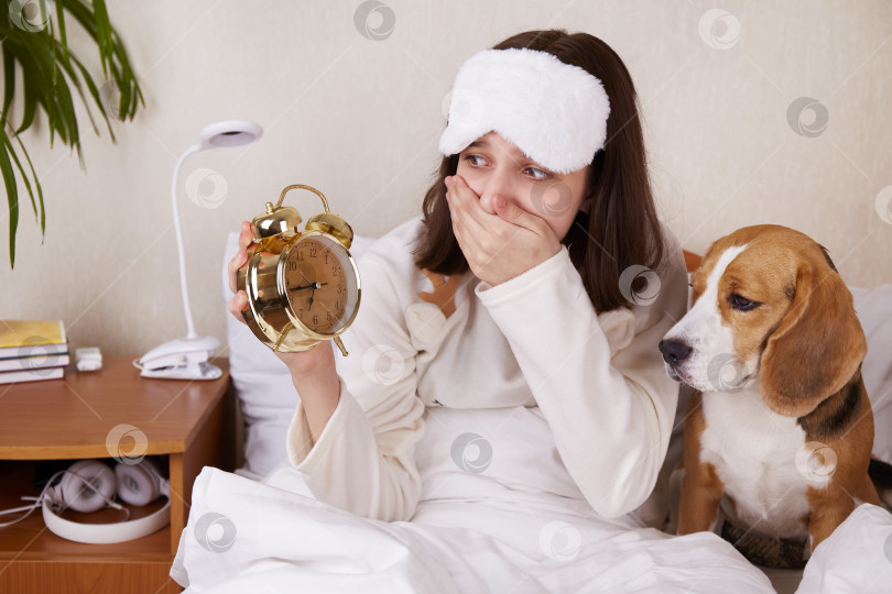 Скачать Утром удивленная девушка смотрит на будильник. Сижу в постели в пижаме и маске. фотосток Ozero